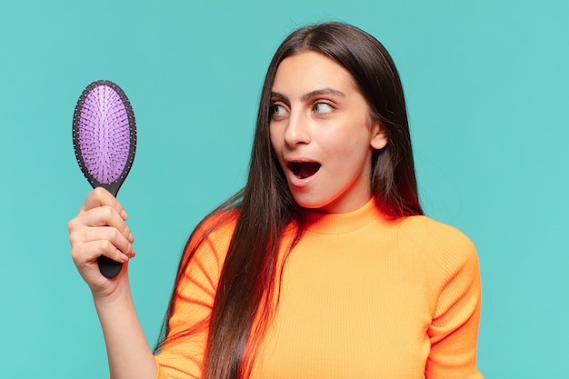 Mulher jovem e bonita com expressão de choque ou surpresa segurando uma escova de cabelo