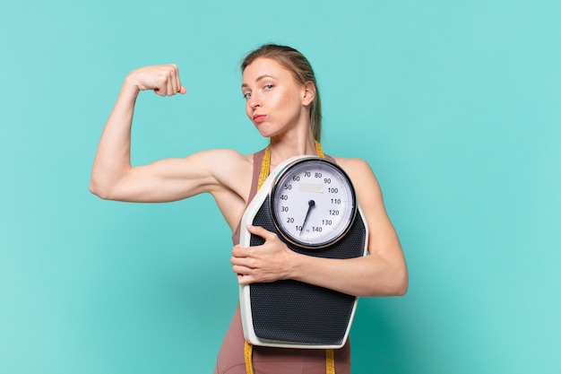 Mulher jovem e bonita com expressão feliz e segurando uma balança