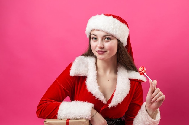 Mulher jovem e bonita com fantasia de Papai Noel contra o fundo vermelho.