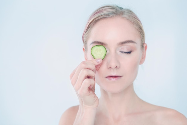 Mulher jovem e bonita com fatias de pepino no fundo branco