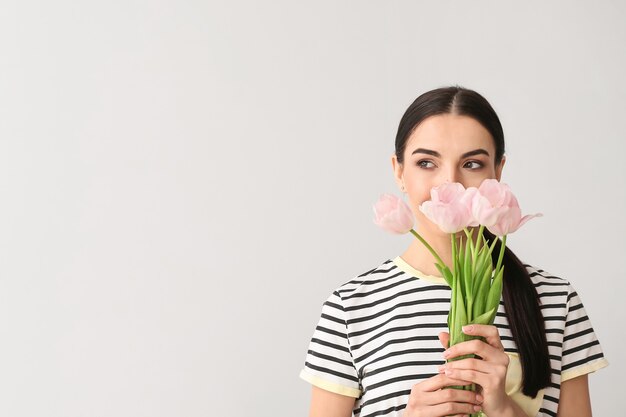 Mulher jovem e bonita com flores na superfície cinza