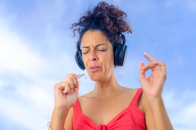 Foto mulher jovem e bonita com fones de ouvido ouvindo música e dançando com o céu ao fundo