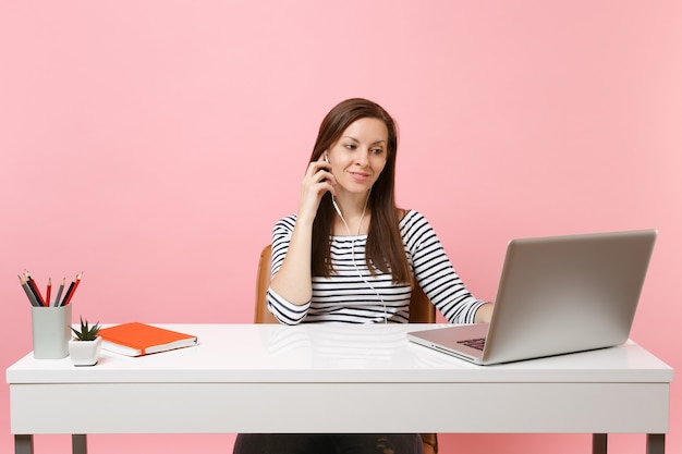 Mulher jovem e bonita com fones de ouvido ouvindo música fazendo videochamada sentar no trabalho no escritório com um laptop pc contemporâneo