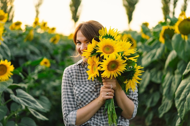 Mulher jovem e bonita com girassóis curtindo a natureza e rindo no campo de girassol de verão