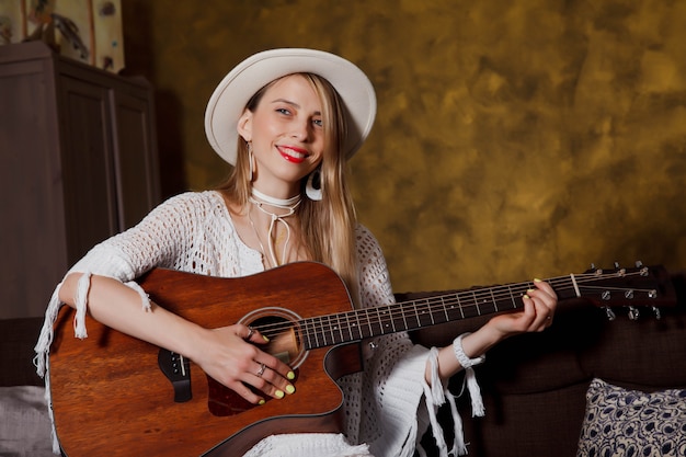 Mulher jovem e bonita com guitarra no interior da sala. Mulher bonita no sofá com o violão nas mãos