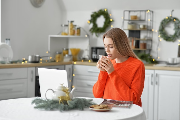 Mulher jovem e bonita com laptop bebendo chocolate quente em casa na véspera de natal