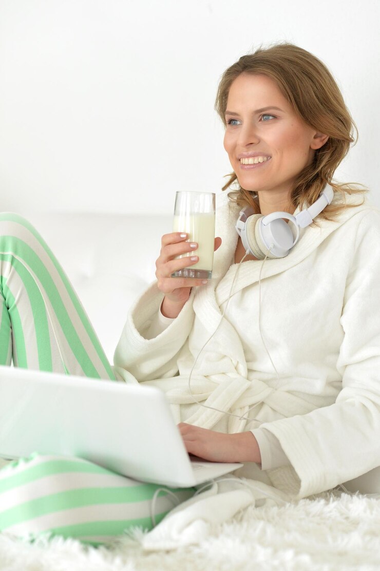 Foto mulher jovem e bonita com laptop sentado na cama com um copo de leite