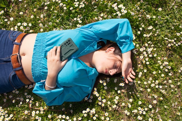 Mulher jovem e bonita com marguerites deitado na grama verde com telefone celular