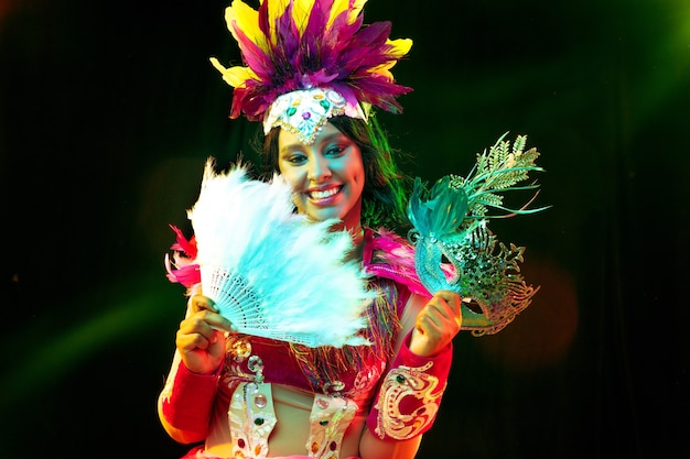 Mulher jovem e bonita com máscara de carnaval e fantasia de baile de máscaras com luzes coloridas