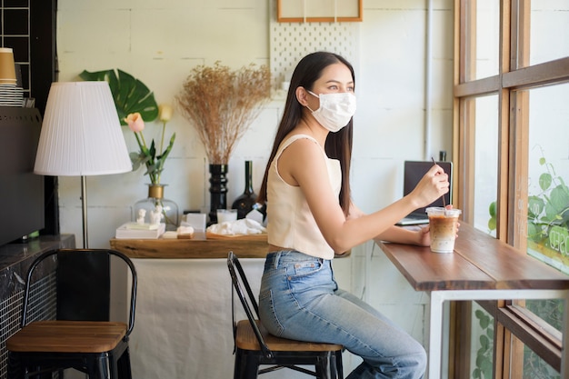 Mulher jovem e bonita com máscara facial está sentado na cafeteria