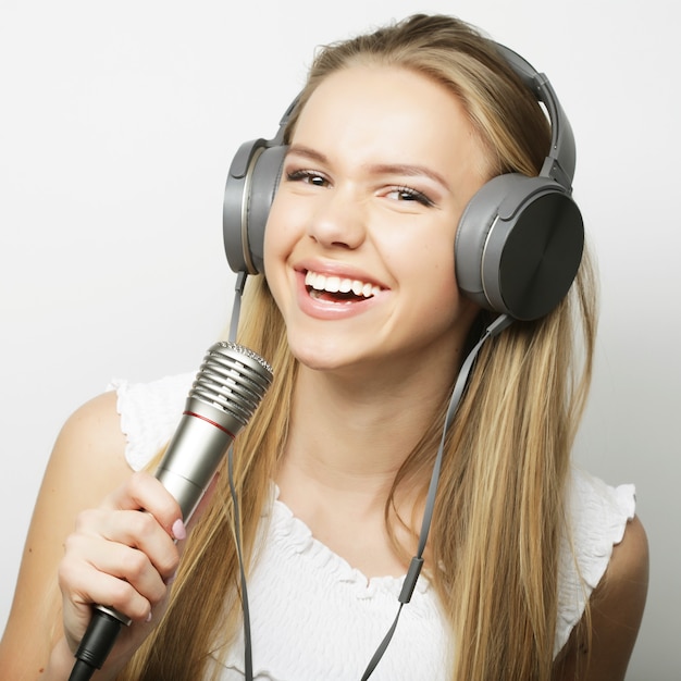 Mulher jovem e bonita com microfone e fones de ouvido em fundo cinza