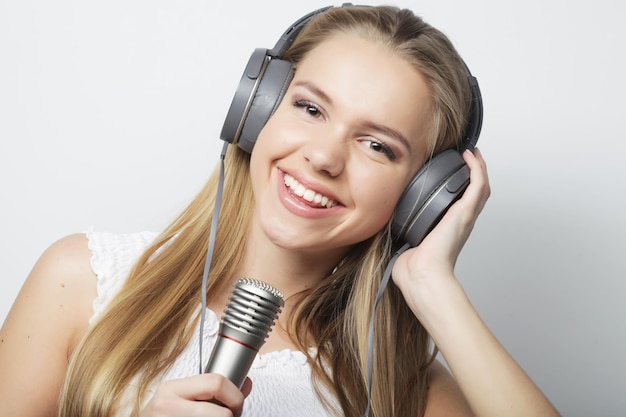 Mulher jovem e bonita com microfone e fones de ouvido em fundo cinza