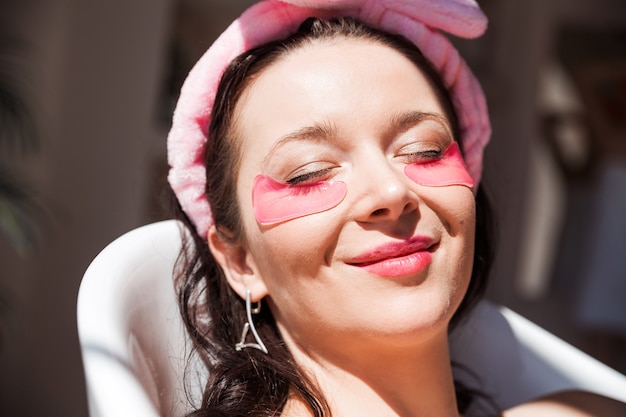 Mulher jovem e bonita com pássaros rosa sob os olhos posa em uma banheira de cerâmica branca