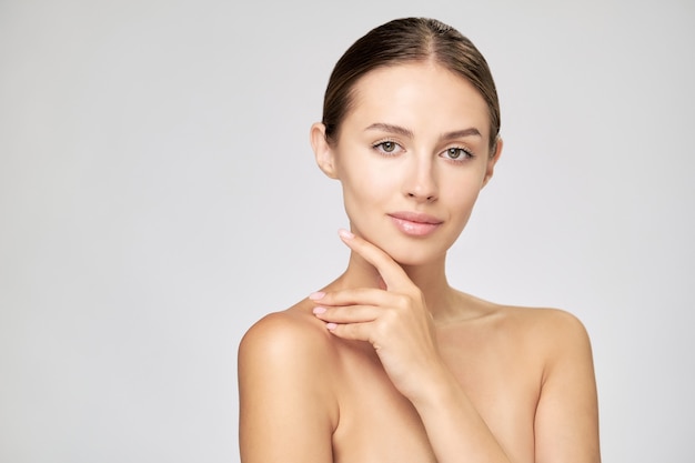 Mulher jovem e bonita com pele limpa e fresca em pé sobre um fundo cinza claro