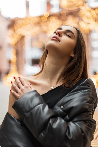 Mulher jovem e bonita com pele limpa e fresca em uma jaqueta preta da moda e top senta-se na rua e acaricia a pele do ombro