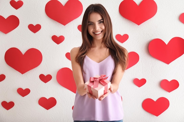 Mulher jovem e bonita com presente para o dia dos namorados perto da parede com corações de papel