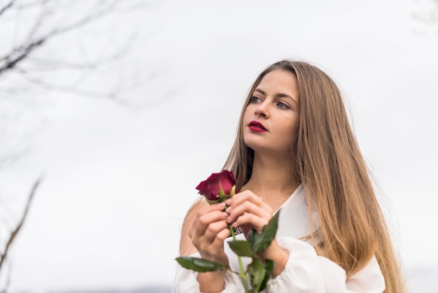 Mulher jovem e bonita com rosa vermelha posando ao ar livre