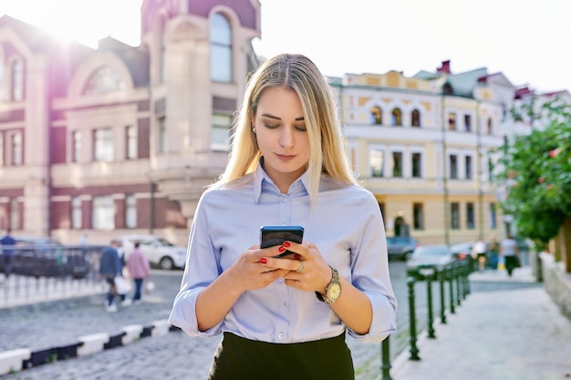 Mulher jovem e bonita com smartphone digitando texto fundo de rua da cidade tecnologia estilo de vida comunicação conceito de juventude