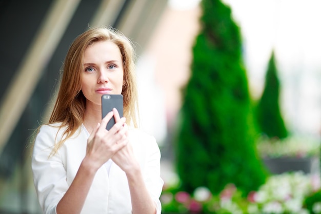 Mulher jovem e bonita com telefone celular. Fundo desfocado da cidade.