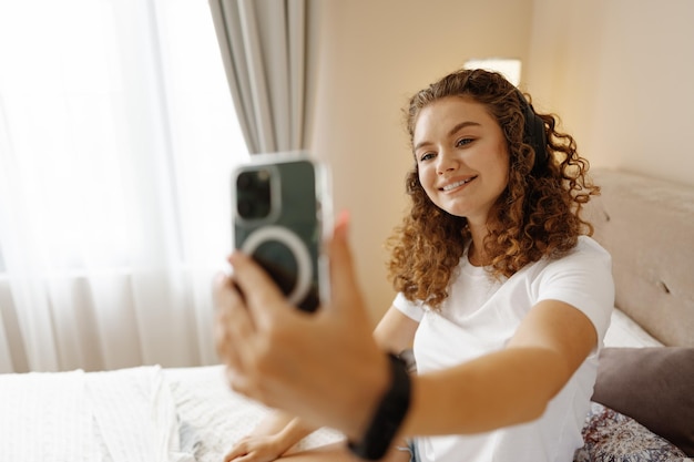 Mulher jovem e bonita com telefone na cama em casa tomando selfie