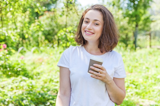 Mulher jovem e bonita com tirar a xícara de café descansando no parque ou jardim