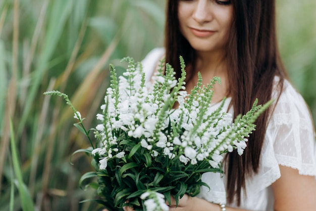 Mulher jovem e bonita com um buquê de flores silvestres com maquiagem ao ar livre