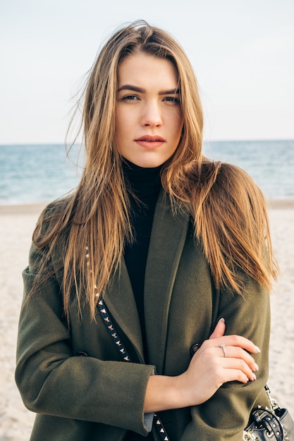 Mulher jovem e bonita com um casaco verde na praia