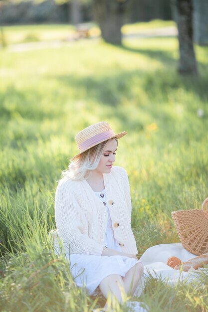 Mulher jovem e bonita com um chapéu de vime descansando em um piquenique em um jardim florido