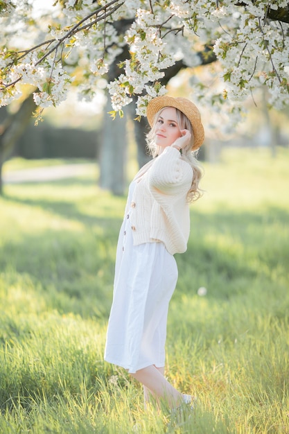 Mulher jovem e bonita com um chapéu de vime está descansando em um piquenique em um jardim florido. Flores brancas. Primavera. Felicidade.