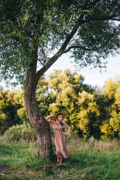 Mulher jovem e bonita com um chapéu e vestido caminha na natureza no outono.