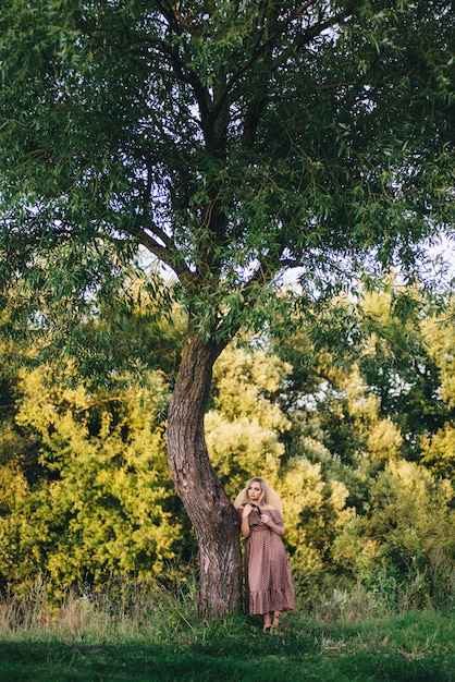 Mulher jovem e bonita com um chapéu e vestido caminha na natureza no outono.