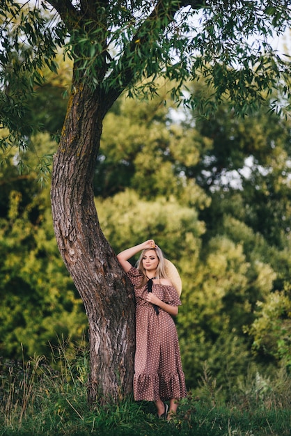 Mulher jovem e bonita com um chapéu e vestido caminha na natureza no outono.