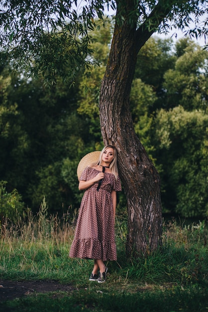 Mulher jovem e bonita com um chapéu e vestido caminha na natureza no outono.