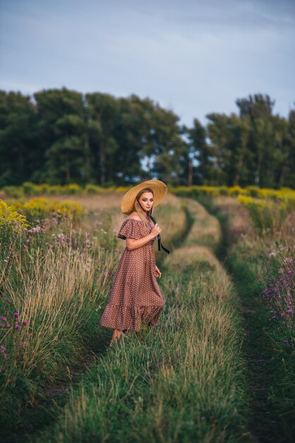 Mulher jovem e bonita com um chapéu e vestido caminha na natureza no outono.