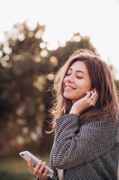 Mulher jovem e bonita com um sorriso ouve e gosta de música do telefone em fones de ouvido na rua