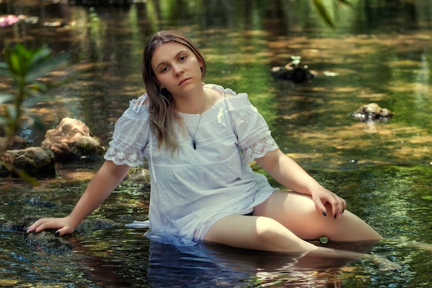 Mulher jovem e bonita com um vestido branco perto do fluxo de água.