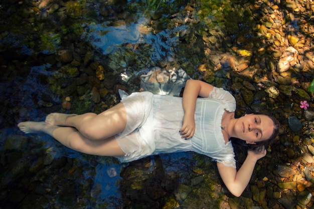 Mulher jovem e bonita com um vestido branco perto do fluxo de água.