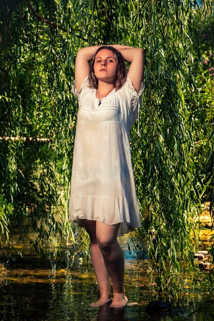 Mulher jovem e bonita com um vestido branco perto do fluxo de água.