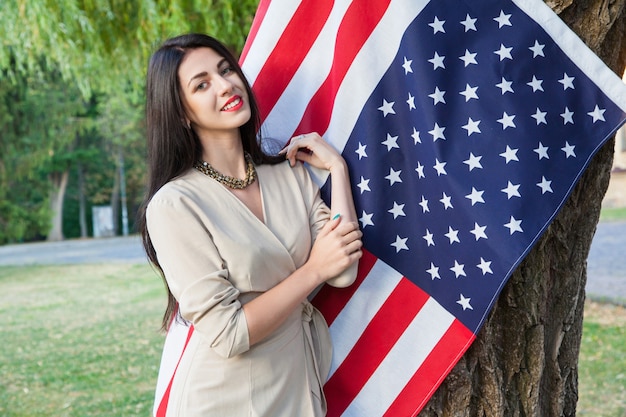 Mulher jovem e bonita com um vestido clássico perto da bandeira americana no parque.