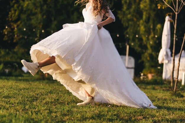 Mulher jovem e bonita com um vestido de casamento branco e botas pretas ao pôr do sol.