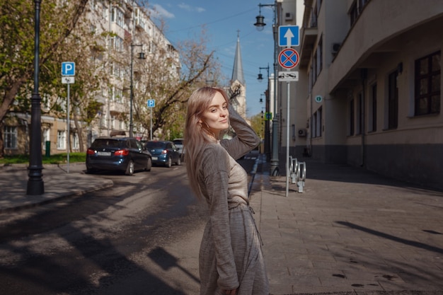 Foto mulher jovem e bonita com um vestido de malha bege caminha pelas ruas de moscou, com o clima ensolarado de primavera