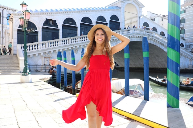 Mulher jovem e bonita com um vestido vermelho caminhando por veneza perto da ponte de rialto, itália