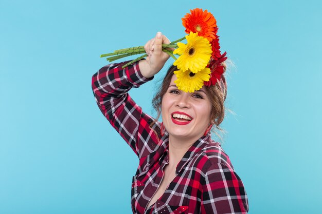 Mulher jovem e bonita com uma camisa xadrez e uma bandagem cheirando uma linda gerbera brilhante