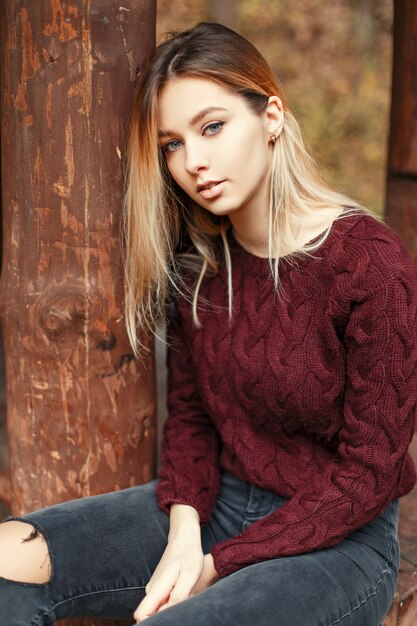 Mulher jovem e bonita com uma camisola da moda sentada perto de uma casa de madeira