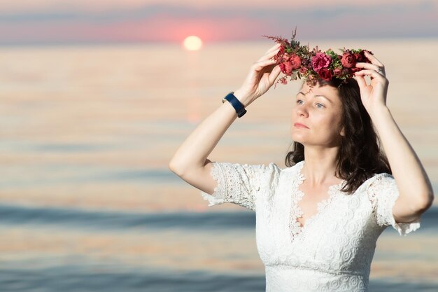 Mulher jovem e bonita com uma coroa de flores na cabeça à beira-mar ao pôr do sol