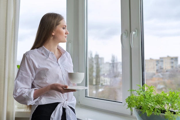 Mulher jovem e bonita com uma xícara de chá em casa perto da janela