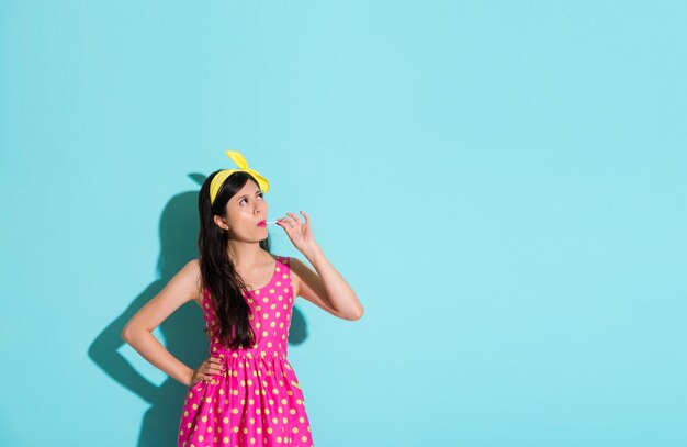 mulher jovem e bonita com vestido bonito em fundo azul e comendo doces de pirulito olhando para a área vazia sonhando acordado.