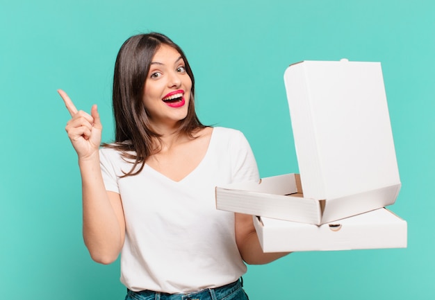 Mulher jovem e bonita comemorando o sucesso de uma vitória e segurando pizzas para levar e segurando pizzas para levar