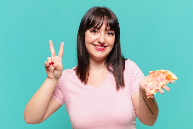 Mulher jovem e bonita comemorando uma vitória bem-sucedida e segurando uma pizza