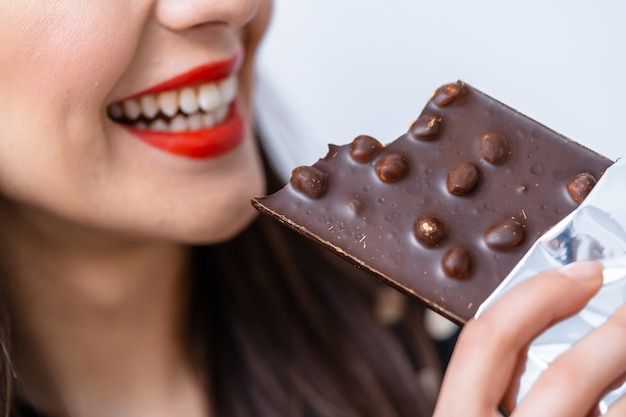 Mulher jovem e bonita comendo uma barra de chocolate com nozes. Fechar-se. Lábios vermelhos.